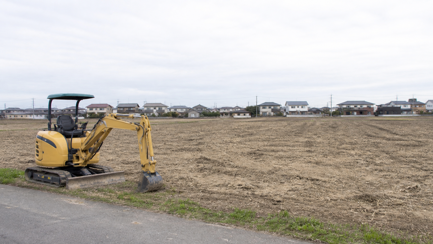 宅地への造成が始まる前の平坦な畑と小型の建設重機のイメージ